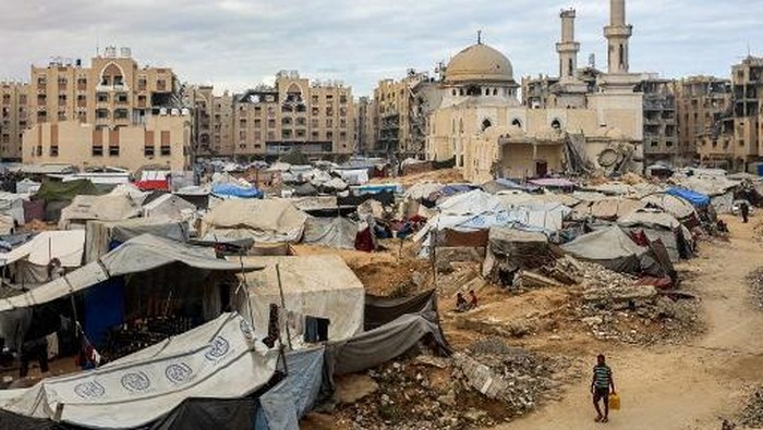 A man carries a jerrycan as he walks past tents sheltering people displaced by war pitched near the heavily-damaged Sheikh Hamad bin Khalifa Al-Thani mosque at the Qatari-built Hamad City residential complex in northwestern Khan Yunis, in the southern Gaza Strip, on October 6, 2025. Delegations from Hamas, Israel and the United States are holding talks in Egypt on October 6, with President Donald Trump urging negotiators to 