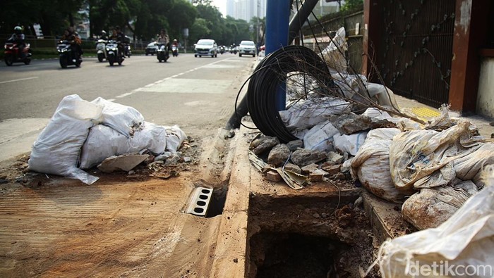 Tiang Miring dan Kabel Kusut Warnai Proyek Trotoar Tebet Warga melintas di antara kabel fiber yang menjuntai dari tiang yang miring dan nyaris ambruk di Jl Abdullah Syafei, Tebet, Jakarta Selatan, Rabu (8/10/2025). Tampak bagian bawah berupa jalur pedestrian yang masih dalam tahap akhir revitalisasi (belum selesai sepenuhnya).