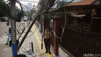Warga berjalan di bawah tiang miring dengan kabel fiber yang menjuntai di Jalan Abdullah Syafei, Tebet, Jakarta Selatan, Rabu (8/10/2025).