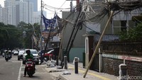 Sejumlah kabel menjuntai rendah dan tiang miring di atas trotoar, menimbulkan potensi bahaya bagi pejalan kaki di sekitar kawasan proyek.