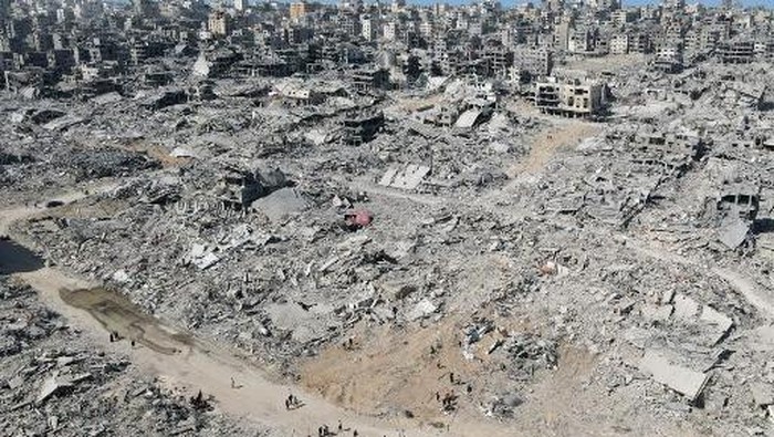 In this aerial view, People walk amid the destruction in Gaza City in the northern Gaza Strip on October 11, 2025, a day after a ceasefire took effect. Israel declared a ceasefire in Gaza and began to pull back its forces on October 10, as tens of thousands of exhausted Palestinians made their way back to their devastated homes. (Photo by AFP)