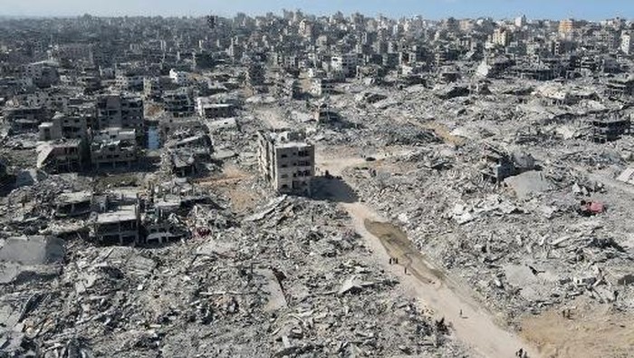In this aerial view, People walk amid the destruction in Gaza City in the northern Gaza Strip on October 11, 2025, a day after a ceasefire took effect. Israel declared a ceasefire in Gaza and began to pull back its forces on October 10, as tens of thousands of exhausted Palestinians made their way back to their devastated homes. (Photo by AFP)