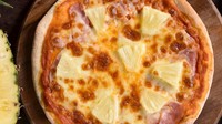 Dikenal sebagai pizza yang kontroversial, Hawaiian Pizza identik dengan topping potongan nanas di atasnya. Tetapi pizza ini ternyata datang dari Kanada, bukan Hawai. Foto: TasteAtlas