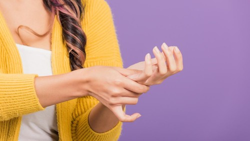 Portrait of Asian beautiful young woman suffering from pain in palm or hands and massaging her painful hands, studio shot isolated on purple background, Health care arthritis concept