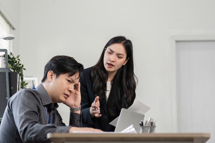A female professional expresses concern as her male colleague shows signs of stress during a project discussion, emphasizing workplace dynamics.