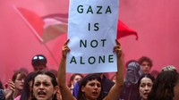 Seorang peserta aksi mengangkat poster di depan bendera Palestina yang berkibar di Barcelona, Spanyol, Rabu (15/10/2025). Simbol-simbol ini mempertegas pesan solidaritas untuk warga Gaza. REUTERS/Albert Gea  