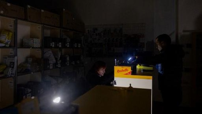 A national postal service of Ukraine worker uses a flashlight to serve a customer during a power outage in Kyiv, on October 16, 2025, amid the Russian invasion of Ukraine. (Photo by Tetiana DZHAFAROVA / AFP)