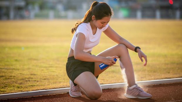 1208757386 Asian Sports women using freezing spray for treating injured sportwomen's knee and leg  after run