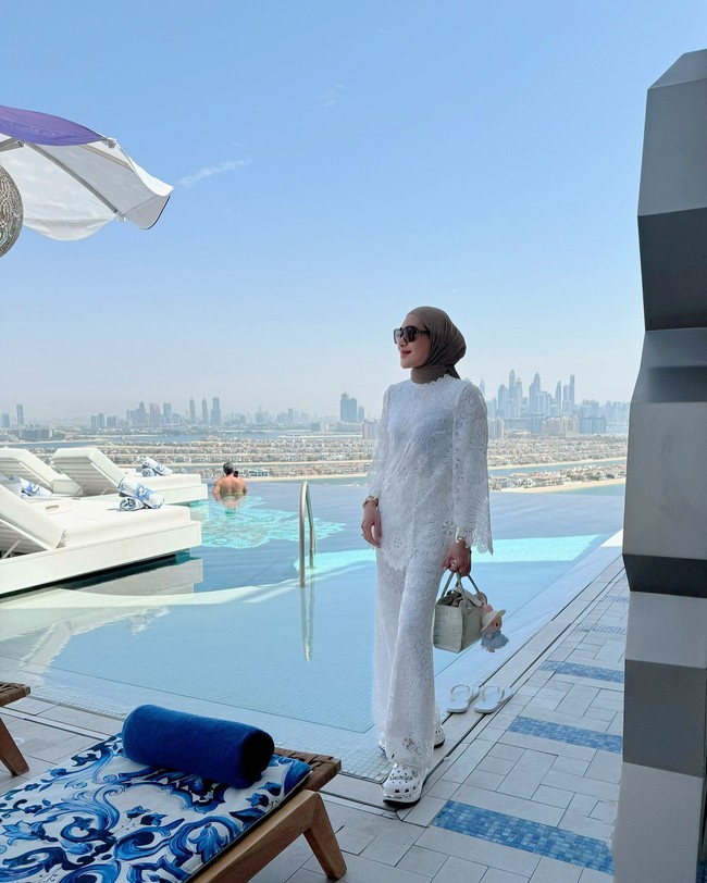 Terlepas dari tuduhan hedonisme, dalam sejumlah foto yang diunggah di Instagram, Erin kerap menampilkan gaya modest yang simple namun tetap terkesan elegan. Seperti saat pose di tepi kolam infinity pool, dia mengenakan busana serba putih berbahan lace. Gaya ini tampak segar dan bersih, dilengkapi sandal platform putih dan tas mini bertekstur yang memperkuat kesan resort look. Foto: Instagram/@erintaulany