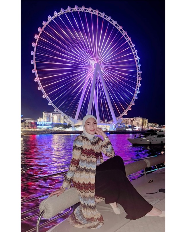 Saat malam hari, Erin mengenakan outer bermotif zigzag bernuansa earthy tone yang flowy, dipadu celana hitam lebar dan hijab putih. Look ini terasa glam namun tetap santai. Foto: Instagram/@erintaulany