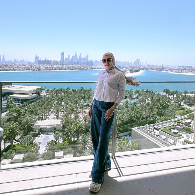 Kemeja putih klasik dan wide-leg jeans menjadi pilihan Erin saat menikmati pemandangan kota. Gaya ini sederhana namun berkelas, dilengkapi aksesori jam tangan emas dan kacamata besar yang memberi sentuhan old-money vibes. Foto: Instagram/@erintaulany