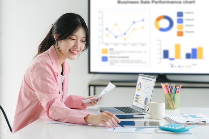 Smiling millennial Asian female office worker working with financial reports for tax audit reports or financial statement in a meeting room