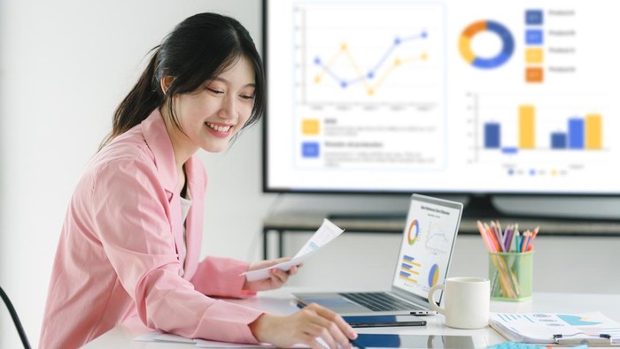 Smiling millennial Asian female office worker working with financial reports for tax audit reports or financial statement in a meeting room