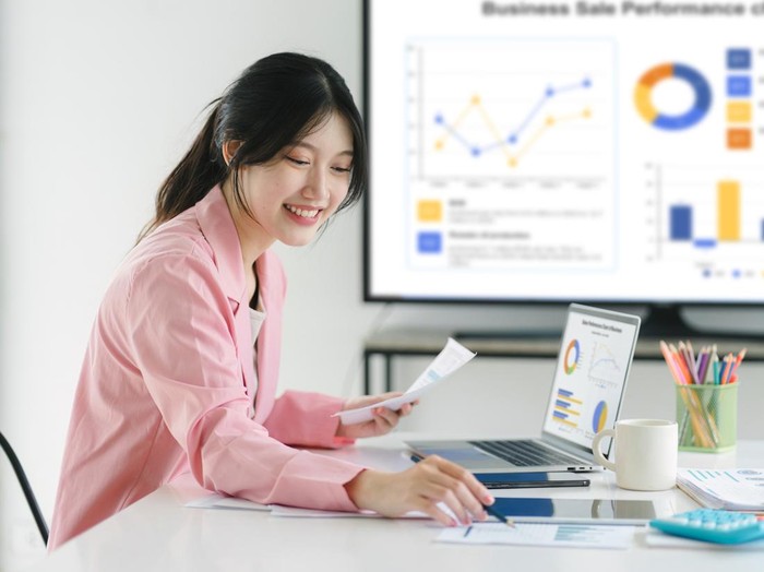 Smiling millennial Asian female office worker working with financial reports for tax audit reports or financial statement in a meeting room