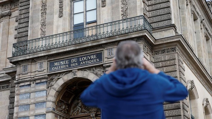 Lokasi Pembobolan Louvre Jadi Daya Tarik Wisata Baru di Paris People take a selfie in front of a broken window protected by a wooden panel at the Louvre Museum as the museum remains closed the day after a spectacular jewel heist by thieves who broke into the landmark by using a crane and smashing an upstairs window, stealing priceless jewelry from an area that houses the French crown jewels before escaping on motorbikes, in Paris, France, October 20, 2025. REUTERS/Benoit Tessier TPX IMAGES OF THE DAY