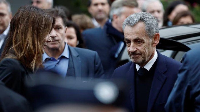 Former French President Nicolas Sarkozy stands next to his wife Carla Bruni-Sarkozy before leaving in a car on the day of his incarceration at the Sante prison to begin his five-year prison sentence for criminal conspiracy over attempts to raise campaign funds from Libya, in Paris, France, October 21, 2025. REUTERS/Benoit Tessier Purchase Licensing Rights