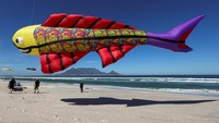 Peserta berlarian di pasir sambil mengendalikan layang-layang mereka, menciptakan suasana ceria di tepi laut Cape Town. REUTERS/Esa Alexander