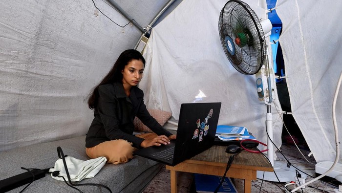 Perjuangan Siswa Palestina Lulus Sekolah di Tengah Perang Gaza Palestinian student Raghad Loai Mhanna, who passed her high school exams while living in a tent after being displaced during the war, works on her laptop inside her tent in Deir al-Balah, central Gaza Strip, October 19, 2025. REUTERS/Mahmoud Issa