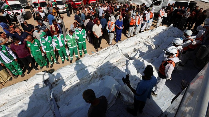 Pilu Warga Gaza Makamkan Puluhan Jenazah Tak Dikenal yang Diserahkan Israel Palestinians gather near the unidentified bodies as they prepare them for burial at a mass burial site, after they were handed over by Israel, amid a ceasefire between Israel and Hamas, at Nasser Hospital in Khan Younis in the southern Gaza Strip, October 22, 2025. REUTERS/Ramadan Abed