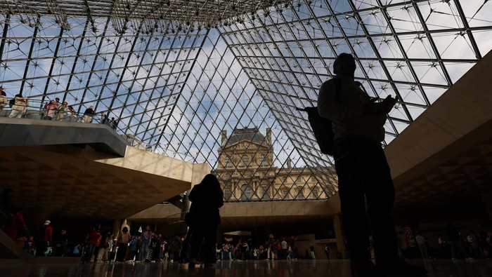 Potret Museum Louvre Kembali Dibuka Usai Pencurian Perhiasan Bernilai Fantastis Visitors walk below the glass Pyramid at the Louvre Museum on the day it reopened to the public for the first time since last Sunday's heist, while the Galerie d'Apollon where eight pieces of Napoleon and the Empress's jewelry collection displayed in the gallery were stolen by thieves, remains closed, in Paris, France, October 22, 2025. REUTERS/Gonzalo Fuentes