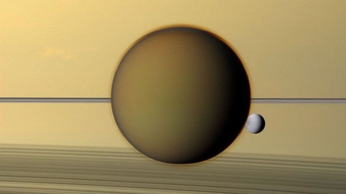 Titan (tengah), dan sesama bulan Dione (kanan), melintas di depan Saturnus dan cincinnya (latar belakang).