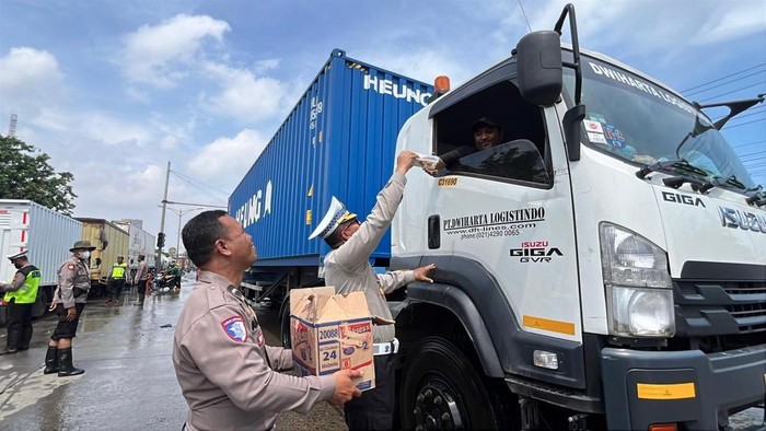 Personel Satlantas Polrestabes Semarang saat membagikan makanan dan minuman kepada para sopir truk yang berhenti akibat banjir di kawasan Kaligawe, Jumat (24/10/2025).