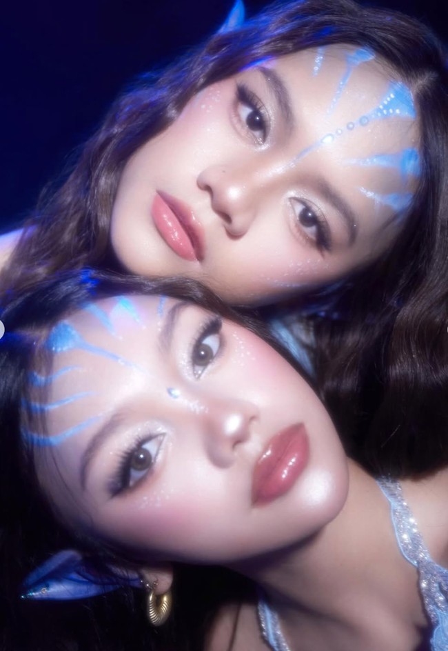 Kedua kakak beradik ini tampil dengan riasan wajah dari MUA @mimi.mua.mua. Sentuhan garis biru di dahi dan pipi menyerupai pola khas bangsa Na’vi dalam film Avatar. Highlight berkilau di pipi dan kelopak mata memberi kesan, seolah kulit mereka bercahaya. Foto: Instagram/@naura.ayu