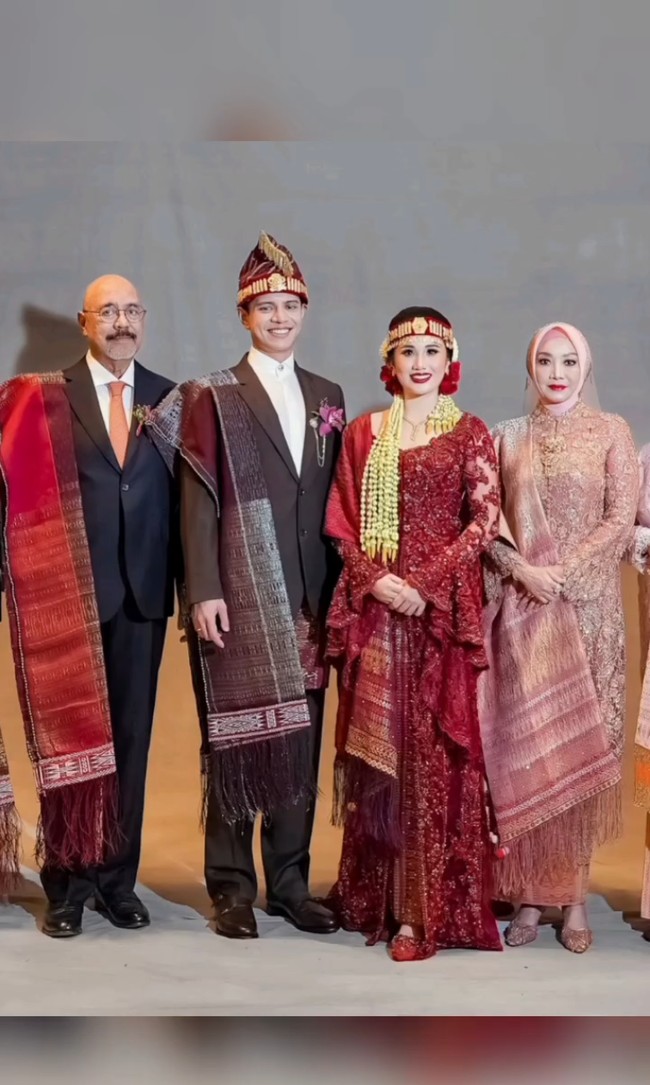 Mempelai pria Moshe Panjaitan memakai setelah jas yang dipadukan kemeja kerah tinggi. Putra tunggal dari pengusaha Mahatma Ilham Panjaitan ini memakai Ulos Ragitohang yang disampirkan di bahu kanan. Foto: Instagram/@merdisihombingluxury @myrnamyura