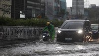Seorang warga mendorong sepeda motor menembus genangan di Jalan Arteri Pondok Indah, Jakarta, Kamis (30/10/2025).