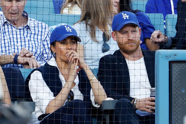 Duduk di barisan depan, Duchess of Sussex tampil santai dengan jeans biru, kemeja putih, dan topi bisbol. Meski berpakaian kasual, ia memastikan wajahnya terpulas optimal. (Foto: Ronald Martinez/Getty Images)