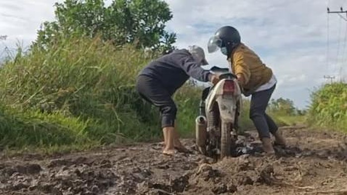 Potret Devi dan rekan kerjanya melalui jalan berlumpur di Desa Bumi Subur.
