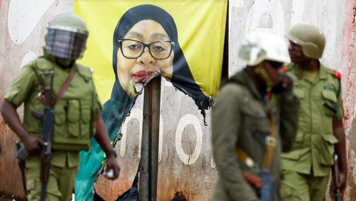 TANZANIA-ELECTION/ Tanzanian riot police officers walk past a vandalised campaign poster of President Samia Suluhu Hassan, following a protest a day after a general election marred by violent demonstrations over the exclusion of two leading opposition candidates at the Namanga One-Post Border crossing point between Kenya and Tanzania, October 30, 2025. REUTERS/Thomas Mukoya
