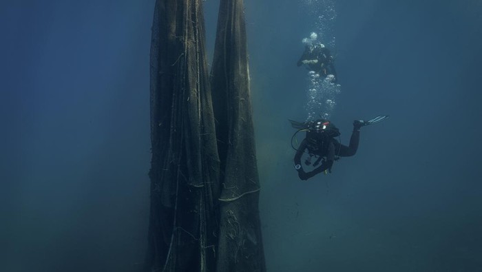 Volunteer divers from the environmental group Aegean Rebreath carry a fish-farming net during an underwater cleanup off the islet of Sapientza, near Methoni, in southern Greece, October 12, 2025. REUTERS/Stelios Misinas