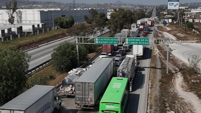 A woman walks past a long line of cargo trucks blocking the Mexico-Queretaro highway as members of transport organizations protest over insecurity, in Tepotzotlan, Mexico, November 3, 2025. REUTERS/Henry Romero
