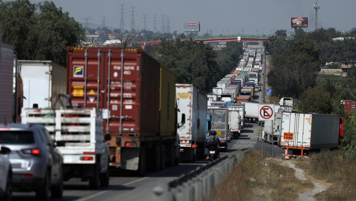A woman walks past a long line of cargo trucks blocking the Mexico-Queretaro highway as members of transport organizations protest over insecurity, in Tepotzotlan, Mexico, November 3, 2025. REUTERS/Henry Romero