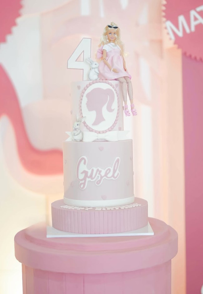 Kue ulang tahun Guzel juga dibuat bertema Barbie dengan warna soft pink. Terdiri dari 3 tingkat, terdapat sebuah boneka Barbie yang diletakkan di sebelah angka 4. Nama Guzel juga turut menghiasi kue ulang tahun tersebut. Foto: Instagram/@marginw
