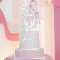 Kue ulang tahun Guzel juga dibuat bertema Barbie dengan warna soft pink. Terdiri dari 3 tingkat, terdapat sebuah boneka Barbie yang diletakkan di sebelah angka 4. Nama Guzel juga turut menghiasi kue ulang tahun tersebut. Foto: Instagram/@marginw
