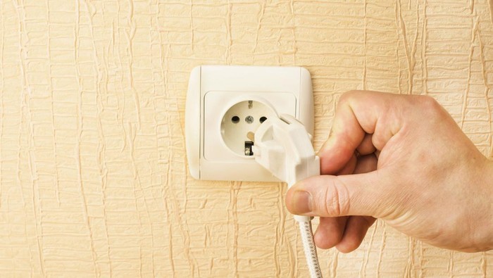 The process of connecting the white plug into the socket on the background of yellow wall