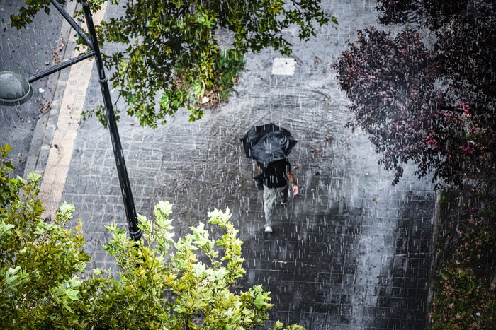 Aerial view of a man with umbrella walking under heavy rain. High resolution 42Mp outdoors digital capture taken with SONY A7rII and Canon EF 70-200mm f/2.8L IS II USM Telephoto Zoom Lens