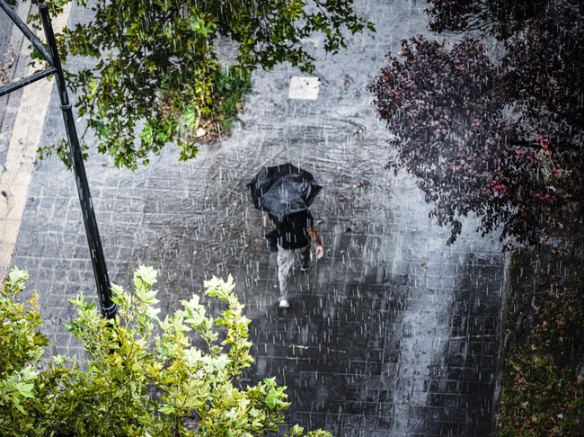 Aerial view of a man with umbrella walking under heavy rain. High resolution 42Mp outdoors digital capture taken with SONY A7rII and Canon EF 70-200mm f/2.8L IS II USM Telephoto Zoom Lens