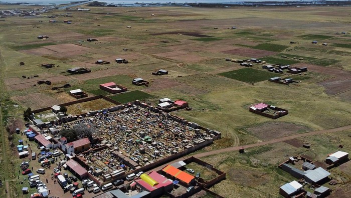 People participating in the traditional All Saints’ Day celebration are reflected on a tomb as Bolivian families prepare offerings with food, flowers, and photos to welcome the souls of their loved ones, in Guaqui, Bolivia November 2, 2025. REUTERS/Claudia Morales     TPX IMAGES OF THE DAY