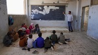 Sejumlah anak duduk di lantai ruang kelas yang rusak di pedesaan Idlib, Suriah. Mereka belajar tanpa meja, kursi, atau papan tulis yang layak setelah 14 tahun perang. Foto: REUTERS/Karam al-Masri