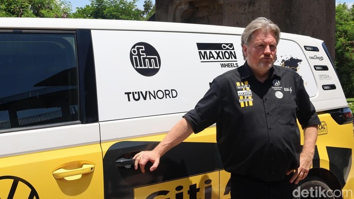 Rainer Zietlow berpose di depan mobil listrik yang dikendarainya dari Jerman hingga tiba di Bali, Selasa (4/11/2025). (Foto: Aryo Mahendro/detikBali)