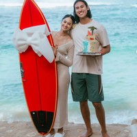 Kue ulang tahun dengan tema pantai terlihat dipegang oleh Sean. Sementara Hana memegang papan surfing merah yang sudah dihias dengan pita putih untuk diberikan kepada Sean sebagai kado ulang tahun. Foto: Instagram/@hanamalasan