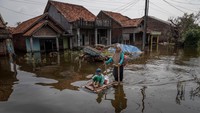Seorang warga menggunakan rakit buatan untuk mengangkut anaknya melintasi banjir yang merendam jalan kampung di Desa Sayung, Demak, Jawa Tengah, Rabu (5/11/2025). ANTARA FOTO/Aji Styawan