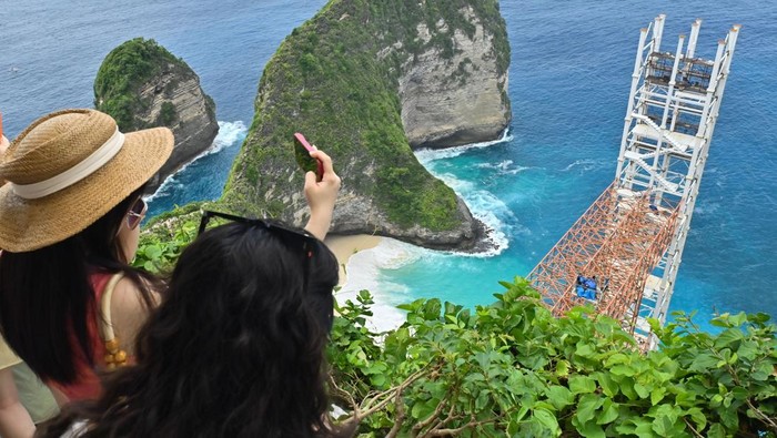 Wisatawan melihat pemandangan di samping bangunan lift kaca di tebing kawasan wisata Pantai Kelingking, Nusa Penida, Klungkung, Bali, Rabu (5/11/2025). Proyek pembangunan lift kaca setinggi 182 meter tersebut dihentikan sementara oleh Panitia Khusus Tata Ruang, Aset, dan Perizinan (Pansus TRAP) DPRD Bali karena dinilai melanggar Undang-Undang Nomor 26 Tahun 2007 tentang Penataan Ruang. ANTARA FOTO/Fikri Yusuf