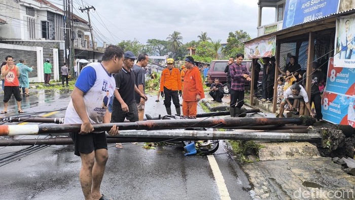 Warga dan petugas gabungan membantu evakuasi sepeda motor yang tertimpa tiang.