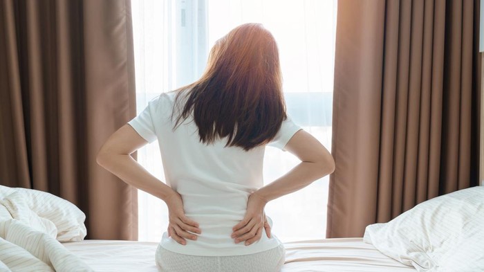 woman having back body ache during sitting on bed at home. adult female with muscle pain after Waking up due to Piriformis Syndrome, Low Back Pain and Spinal Compression. Health medical concept