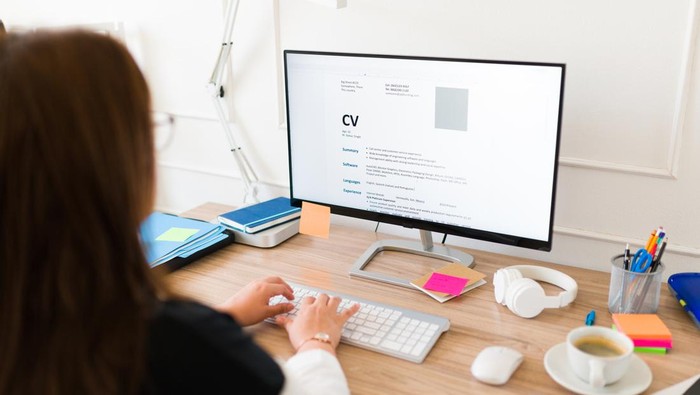 Professional woman seen from behind updating her curriculum or resume on the computer while applying for a new job