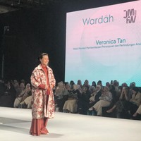 Veronica Tan, Wakil Menteri Pemberdayaan Perempuan dan Perlindungan Anak jadi model di JMFW 2026 mengenakan setelan celana wide-leg pants berwarna terracotta dengan atasan berwarna senada di dalamnya. Statement piece dari outfit ini adalah jaket atau coat panjang berwarna putih dengan motif bunga-bunga merah yang bold. Tampilannya cerah, playful, dan modis. Foto: Gresnia/Wolipop.
